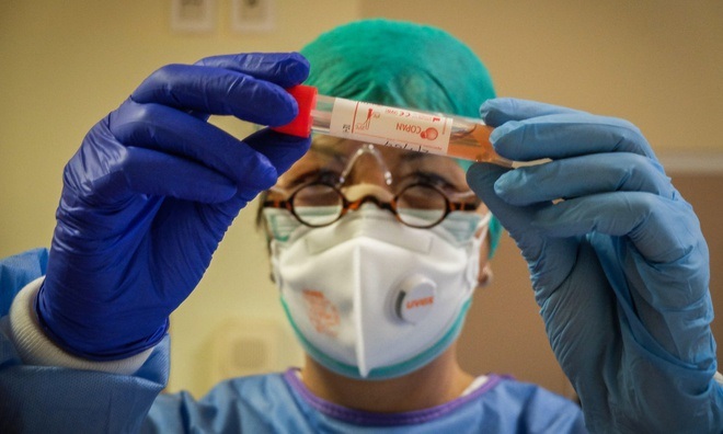 Một chuyên gia chăm sóc sức khỏe kiểm tra một lọ chứa mẫu bệnh phẩm trong phòng xét nghiệm virus corona tại bệnh viện Cremona, Ital (Ảnh: Guardian)