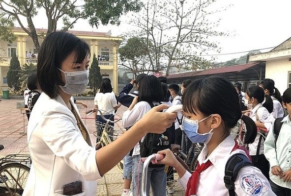 Học sinh thực hiện đeo khẩu trang và đo thân nhiệt trước khi vào trường