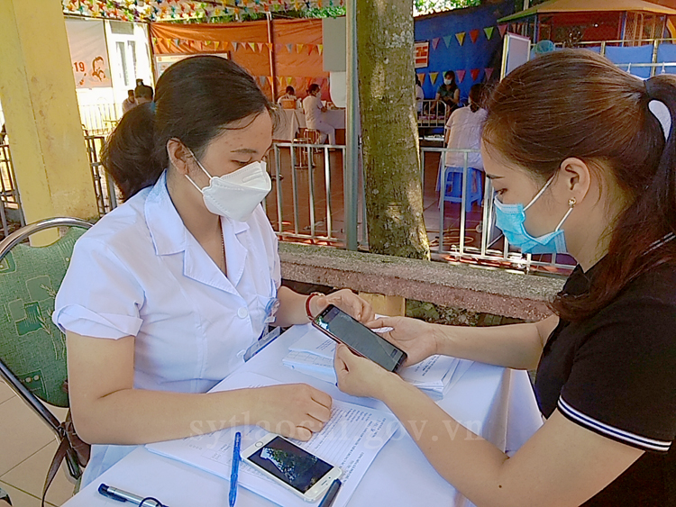 Cán bộ y tế hướng dẫn người dân đến tiêm chủng cài App Sổ sức hỏe điện tử