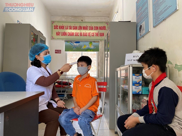 Cán bộ phụ trách y tế của Trường tiểu học Trưng Nhị, thành phố Phúc Yên kiểm tra thân nhiệt cho học sinh. Ảnh: Dương Chung