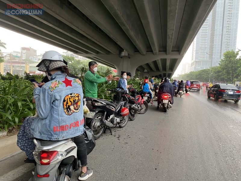 Một số người dân đứng trú mưa dưới chân cầu trên tuyến đường Phạm Văn Đồng