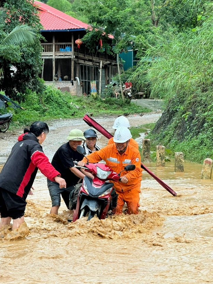 Công nhân Điện lực trên đường đi xử lý sự cố mùa mưa bão được người dân giúp đỡ khi đi qua suối