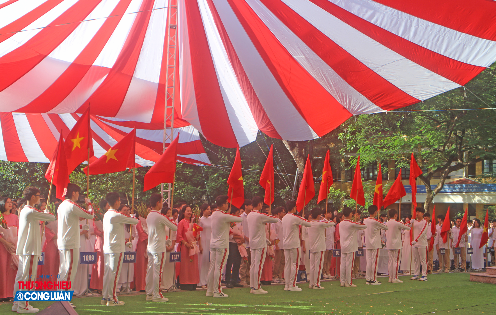 Hình ảnh lá cờ đỏ sao vàng tung bay phía trước, các thầy cô khối lớp 10 trang nghiêm nhận hoa chúc mừng từ đại diện nhà trường.