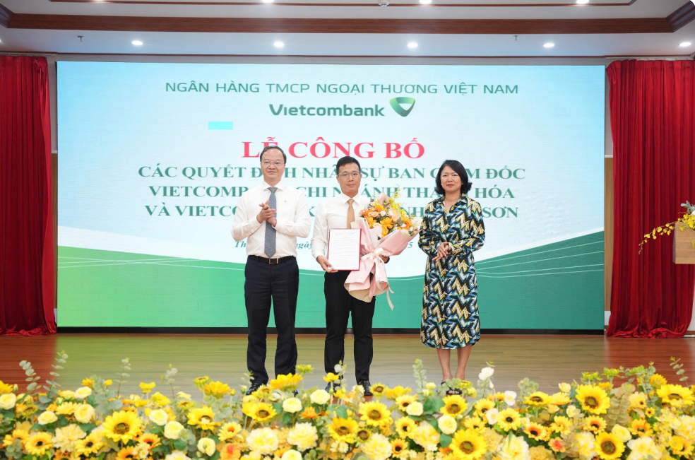 Ông Lê Quang Vinh - Phó Bí thư Đảng ủy, Tổng Giám đốc (bên trái) trao Quyết định và bà Nguyễn Thị Hồng Vân - Giám đốc Khối Pháp chế và Tuân thủ (bên phải) tặng hoa chúc mừng ông Lê Thanh Đức - Phó Giám đốc phụ trách điều hành Vietcombank chi nhánh Nghi Sơn