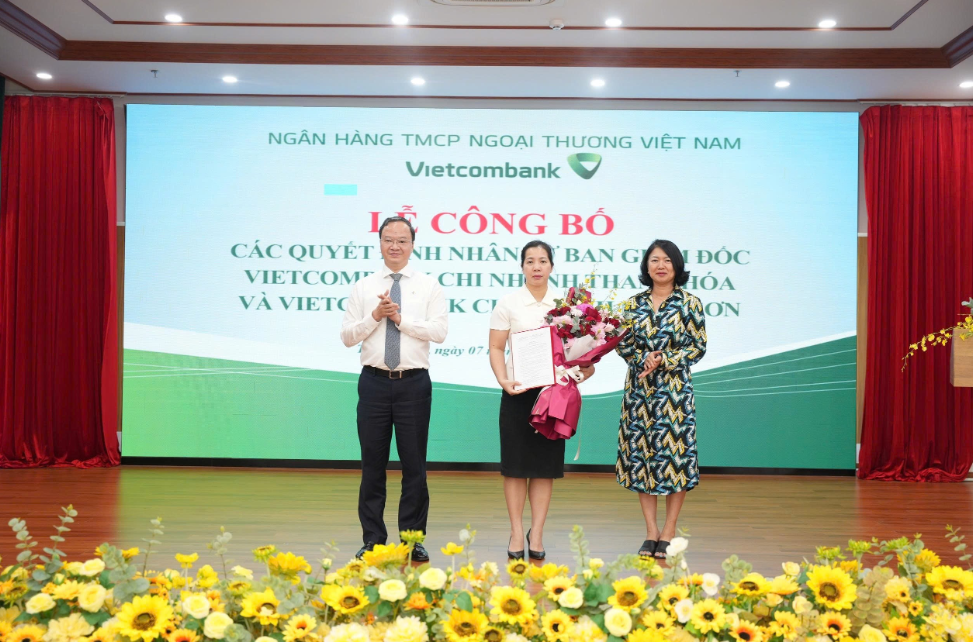 Ông Lê Quang Vinh - Phó Bí thư Đảng ủy, Tổng Giám đốc (bên trái) trao Quyết định và bà Nguyễn Thị Hồng Vân - Giám đốc Khối Pháp chế và Tuân thủ (bên phải) tặng hoa chúc mừng bà Lê Thị Hiền - tân Bí thư Chi bộ, Giám đốc Vietcombank chi nhánh Thanh Hóa