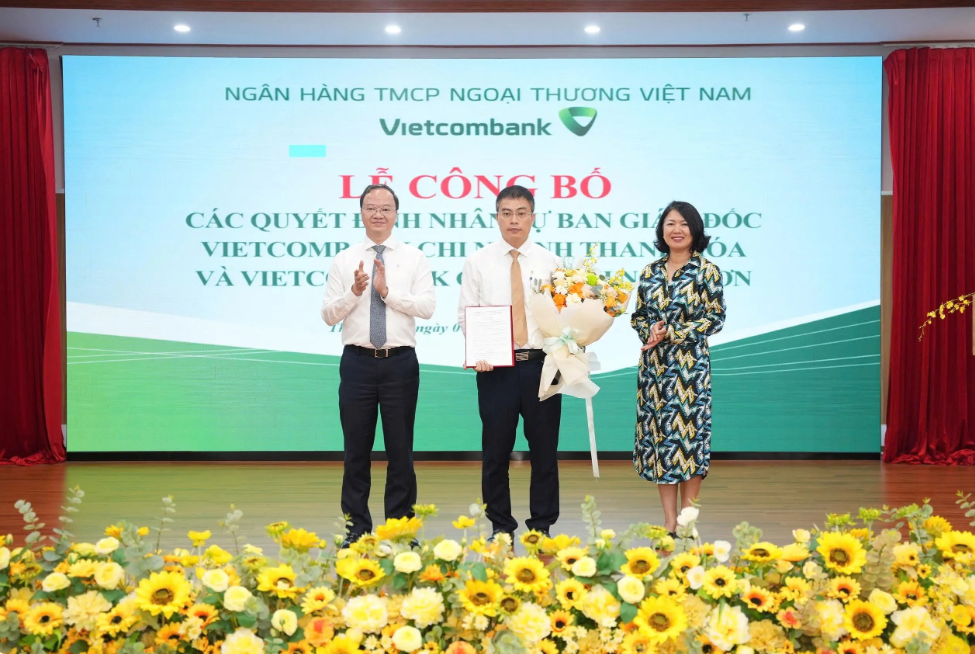 Ông Lê Quang Vinh - Phó Bí thư Đảng ủy, Tổng Giám đốc (bên trái) trao Quyết định và bà Nguyễn Thị Hồng Vân - Giám đốc Khối Pháp chế và Tuân thủ (bên phải) tặng hoa chúc mừng ông Mai Danh Tiến - tân Phó Giám đốc Vietcombank chi nhánh Nghi Sơn