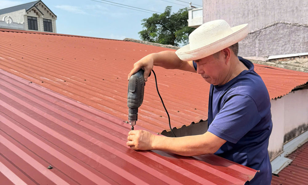 Với những công trình nhà lợp mái tôn, công trình tạm dễ bị tốc mái, hư hại, người dân chủ động đặt các bao cát, túi nước trên mái nhà hoặc bắt vít lại mái tôn cho chắc chắn. Ảnh: Một hộ dân ở phường Chũ gia cố mái tôn.