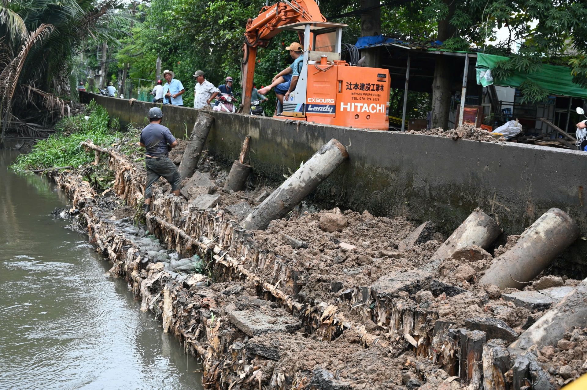Người dân cùng lực lượng địa phương huy động máy xúc, cần cẩu đắp bao cát và gia cố bờ kênh dọc đường Bình Quới (phường Bình Quới, TP. HCM)