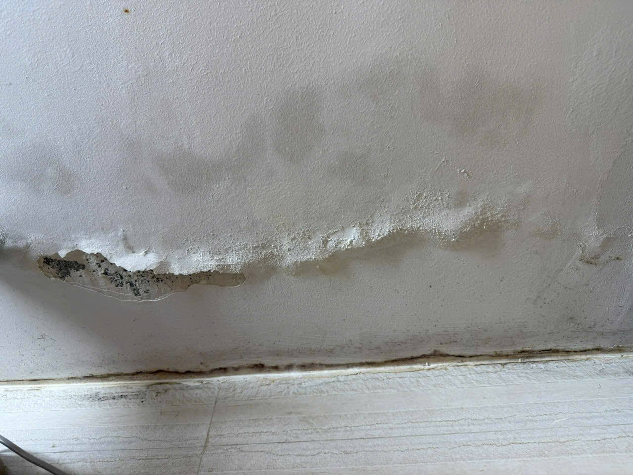 Tường trong căn hộ khu tập thể Nghĩa T&acirc;n bị nổ, bong tr&oacute;c từng mảng lớn do hơi ẩm ngấm s&acirc;u trong nhiều ng&agrave;y nồm, khiến lớp sơn v&agrave; vữa tường bị t&aacute;ch khỏi bề mặt.