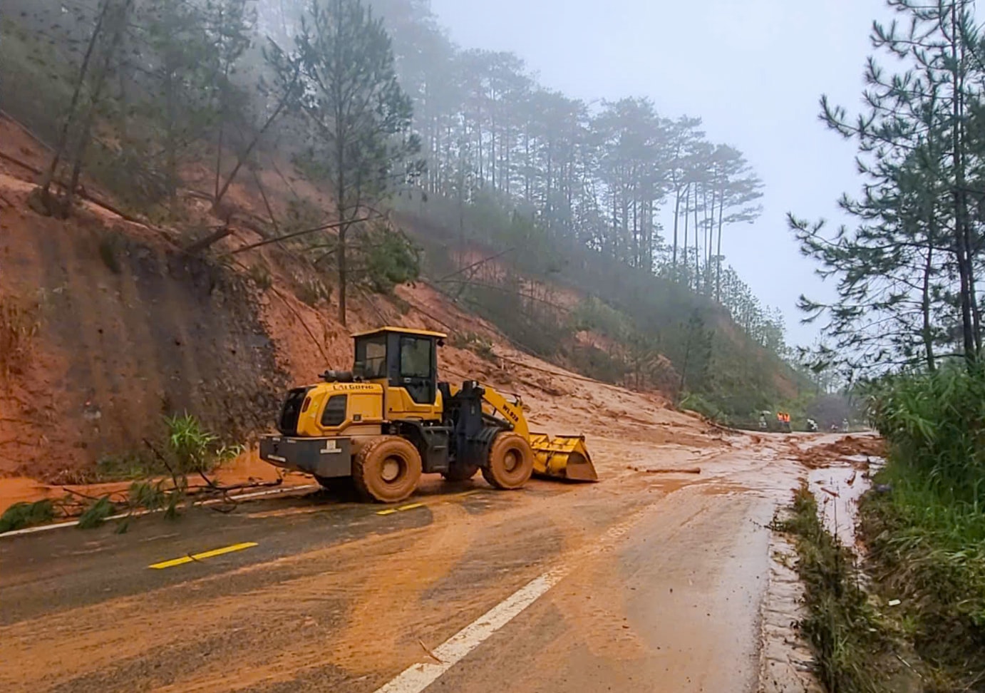 Taluy &acirc;m Km83+750 bị sạt đang được Sở X&acirc;y dựng tổ chức thu dọn đất đ&aacute; tr&agrave;n xuống mặt đường
