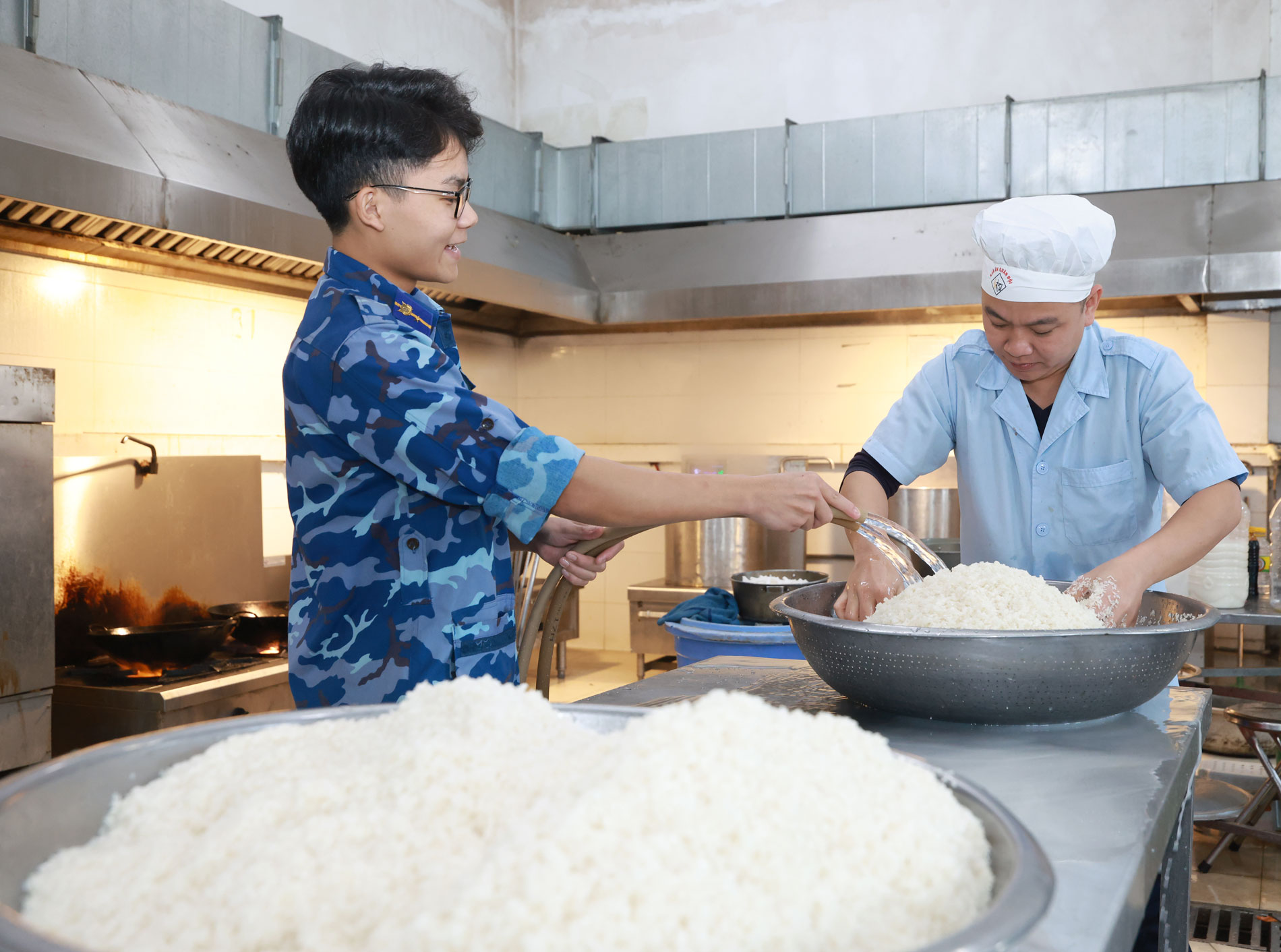 Hạ sĩ Phạm Trọng Đại (đứng) hỗ trợ đồng đội chuẩn bị gạo trước khi cho vào nồi hơi