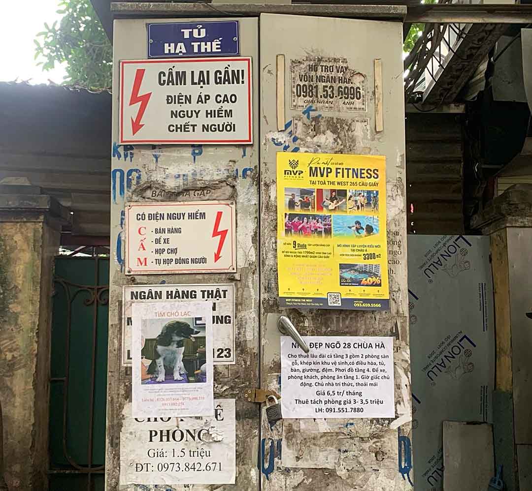 Tờ rơi quảng cáo dán chồng lớp trên cột điện, tạo mảng giấy lộn xộn trên mặt phố.