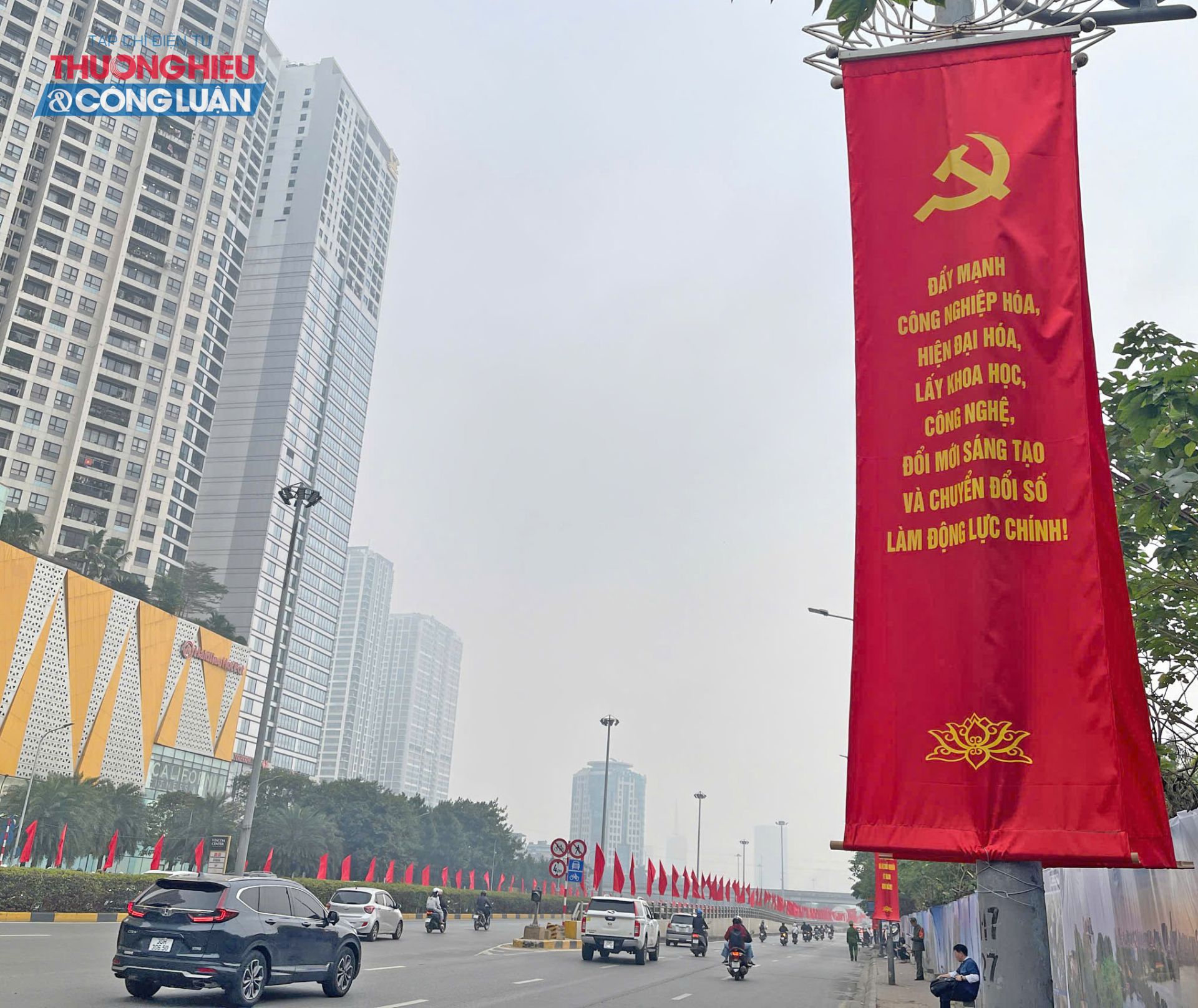 Tr&ecirc;n tuyến đường Trần Duy Hưng dẫn về Trung t&acirc;m Hội nghị Quốc gia sắc đỏ của cờ Đảng, cờ Tổ quốc nổi bật giữa d&ograve;ng xe hối hả.