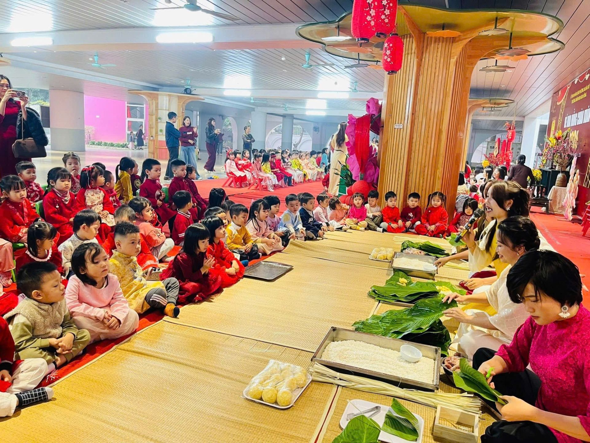Kh&ocirc;ng gian s&acirc;n trường trở th&agrave;nh &ldquo;lớp học Tết&rdquo; khi h&agrave;ng chục trẻ mầm non chăm ch&uacute; theo d&otilde;i v&agrave; tham gia hoạt động g&oacute;i b&aacute;nh chưng.