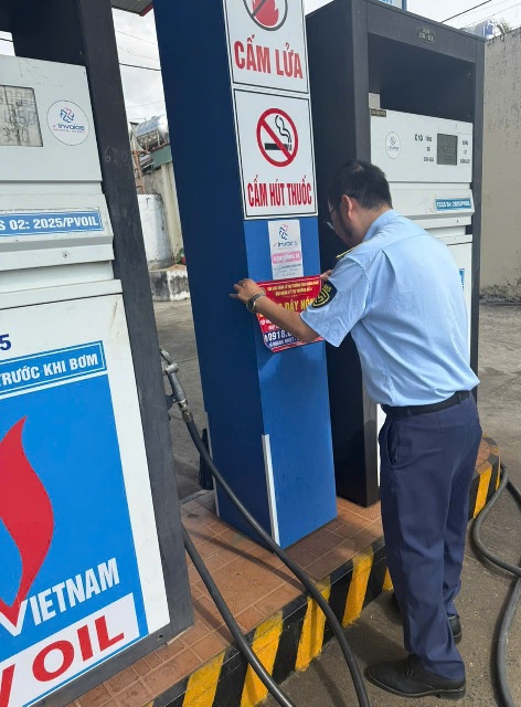 Nh&acirc;n vi&ecirc;n Chi cục QLTT tỉnh Quảng Ng&atilde;i thực hiện việc d&aacute;n số điện thoại &ldquo;đường d&acirc;y n&oacute;ng&rdquo; tại một cửa h&agrave;ng b&aacute;n lẻ xăng dầu. Ảnh: Ngọc Tr&acirc;m