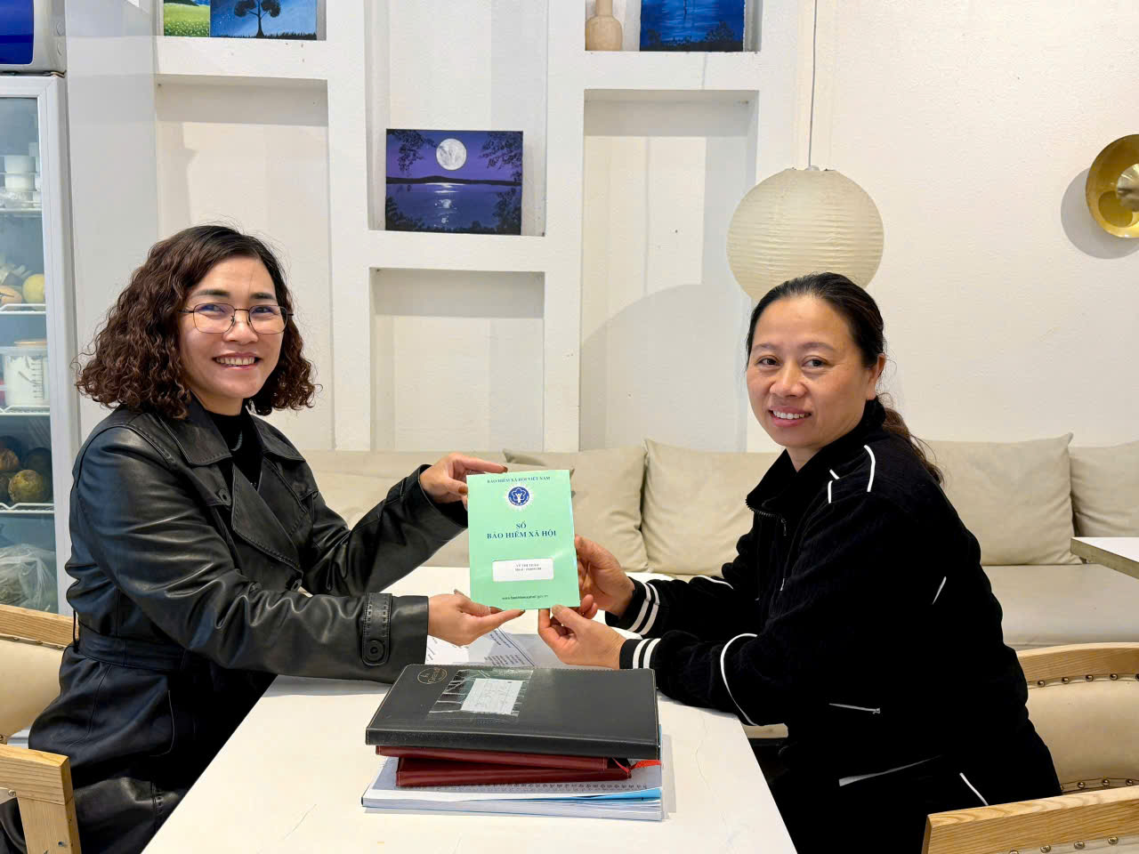 Chị Oanh (b&ecirc;n tr&aacute;i) trao sổ BHXH cho người tham gia BHXH tự nguyện